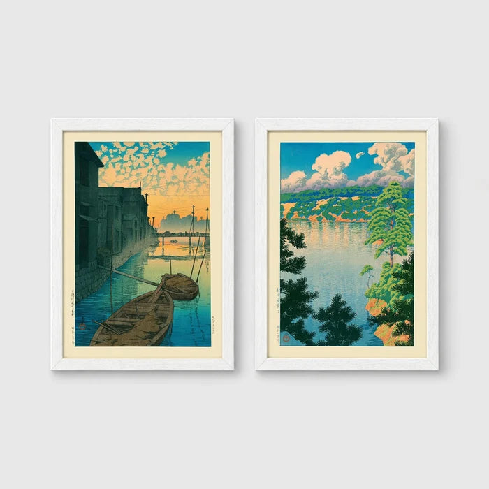 Set of 2 framed prints, Kawase Hasui Japanese woodblock prints: boats moored on a canal at dawn beneath a cloud-streaked sky; and a lake view framed by pine branches beneath drifting clouds — unframed
