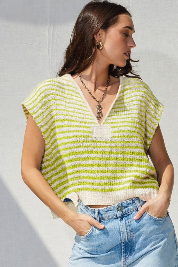 Woman wearing a green and beige striped sleeveless top with blue jeans against a light background