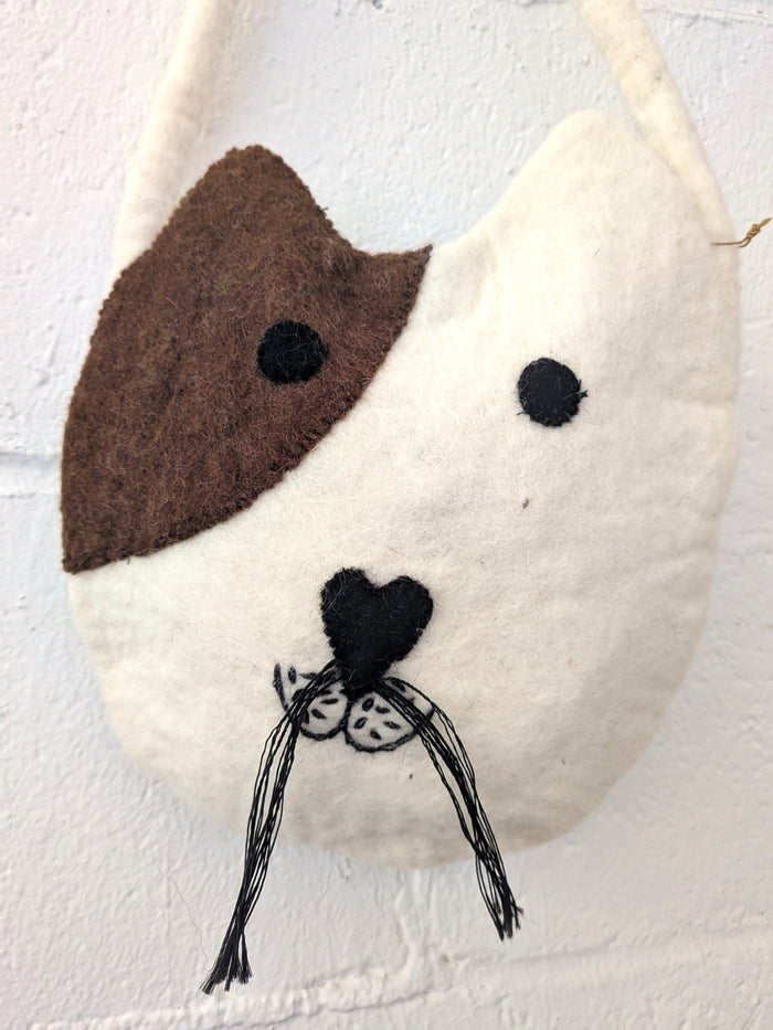 Felt dog-shaped wall hanging with a white body, brown face, and black details on a light gray background.