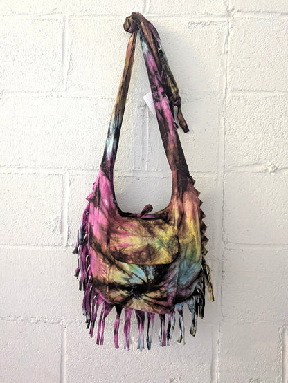 Tie-dye handbag with fringes hanging against a white brick wall.